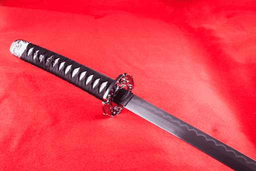 A black and silver samurai sword resting on a vibrant red background.
