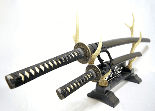 Two samurai swords with decorative antlers displayed on a wooden stand.